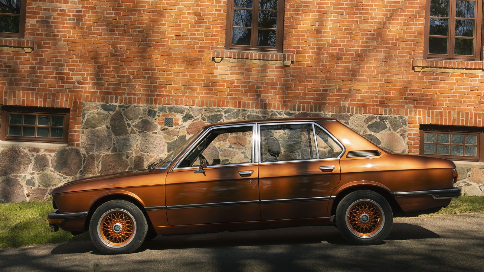 Bronze BMW E28 side profile by a brick building